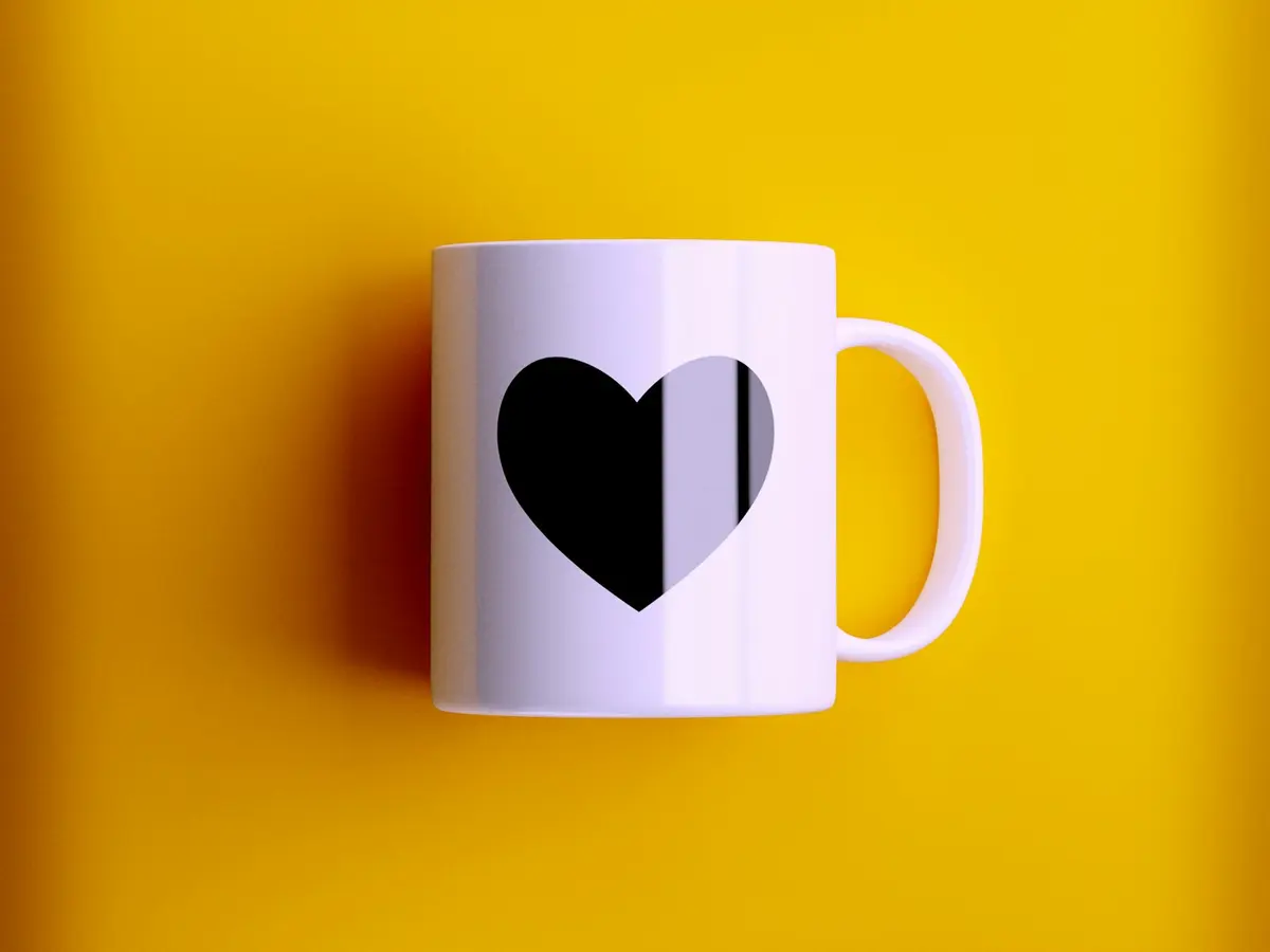 Caneca branca com estampa de coração sobre fundo amarelo